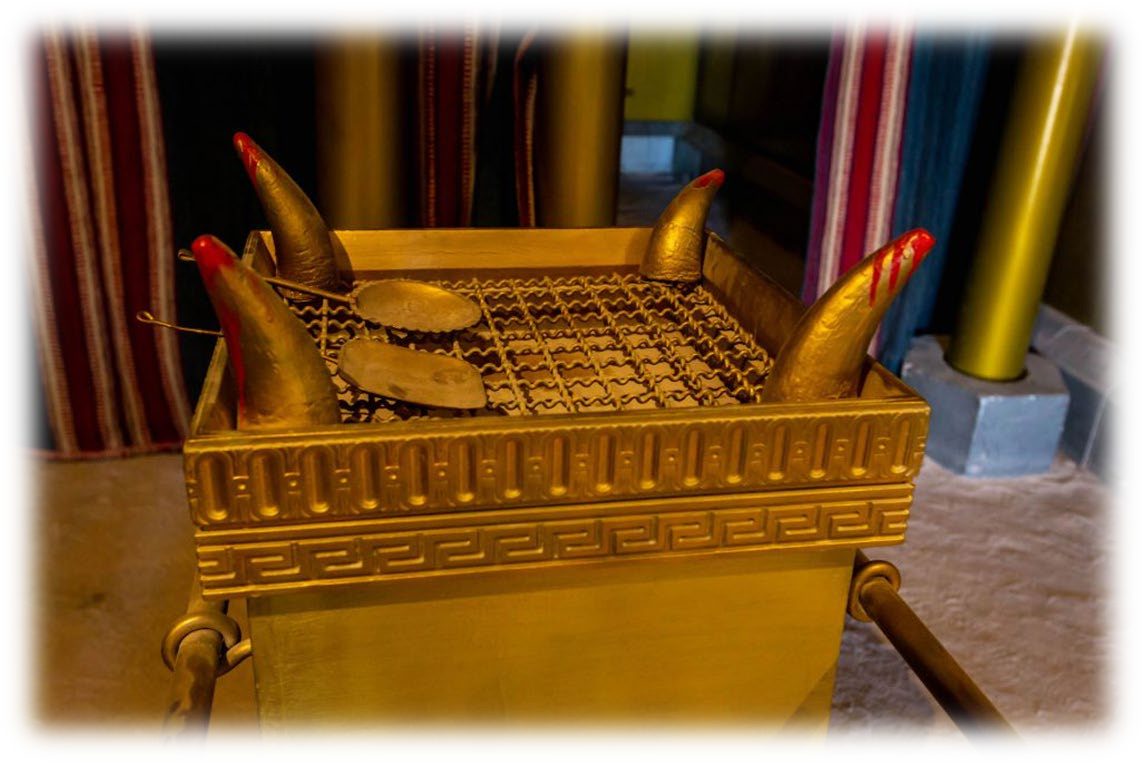 A model of the Brazen Altar with blood on the tips of its four horns, the grate of network on top, a shovel and a pan lying on the grate, and the staves through the rings at its sides