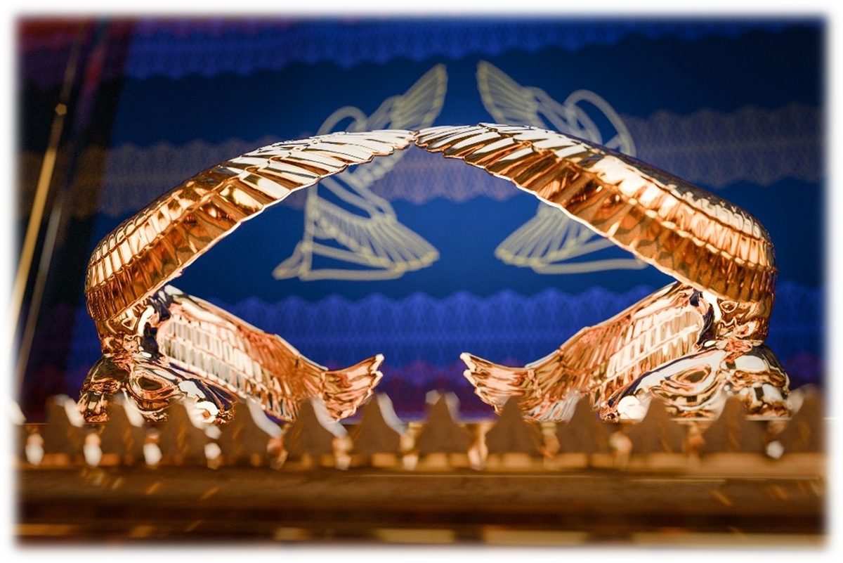 Two golden cherubim with outstretched wings arching over the Mercy Seat, against a blue curtain patterned with cherubim